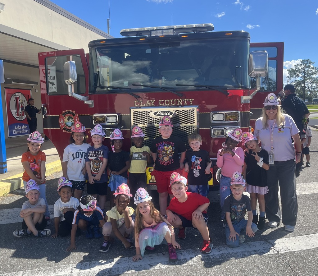 A group of children in hats pose for a photo with a fire truck in the background.