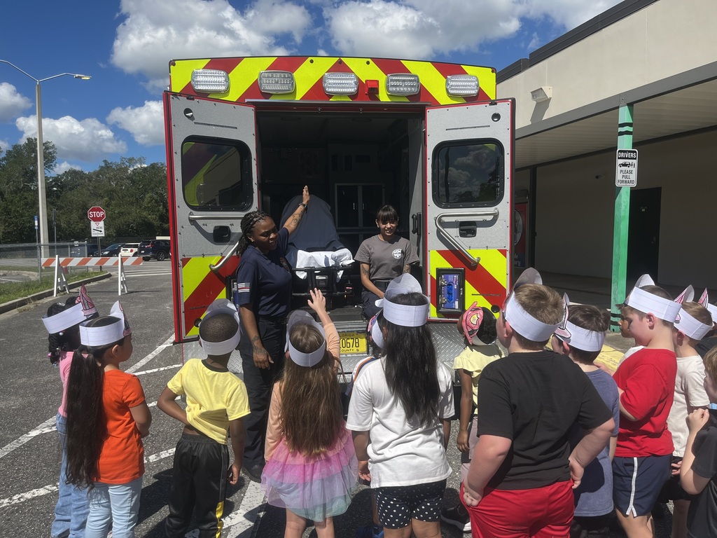 Kids wearing blindfolds gather in a circle around adults in front of an open ambulance.