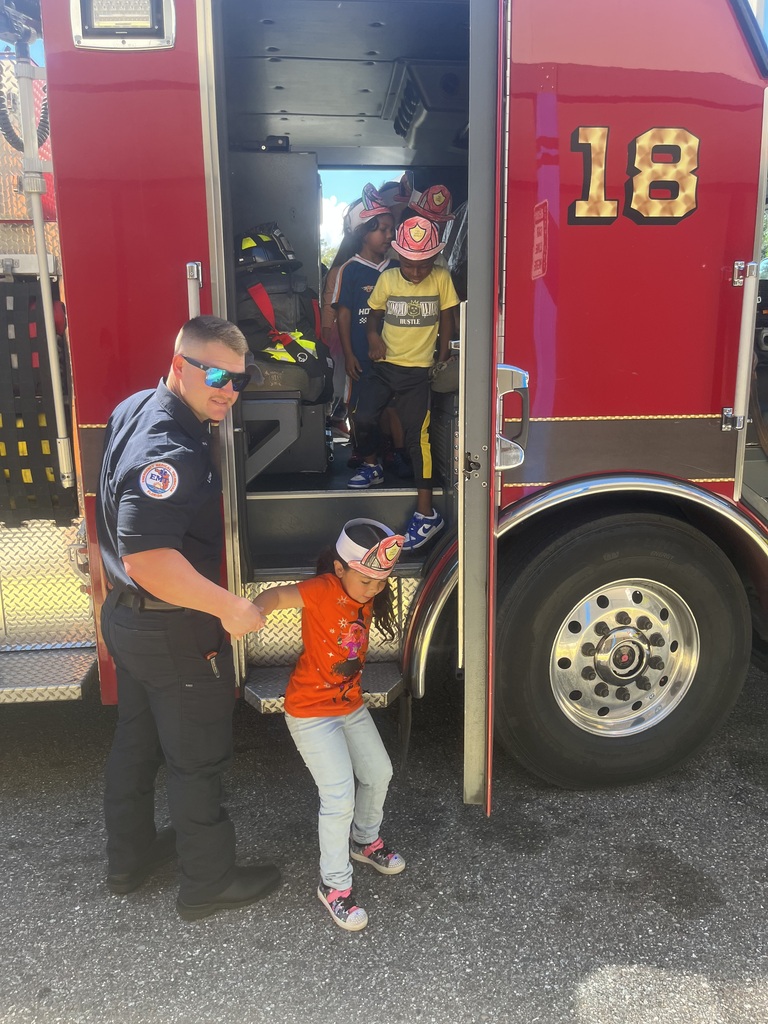 Police officer holding child's hand on ladder, two children standing in open door of firetruck.