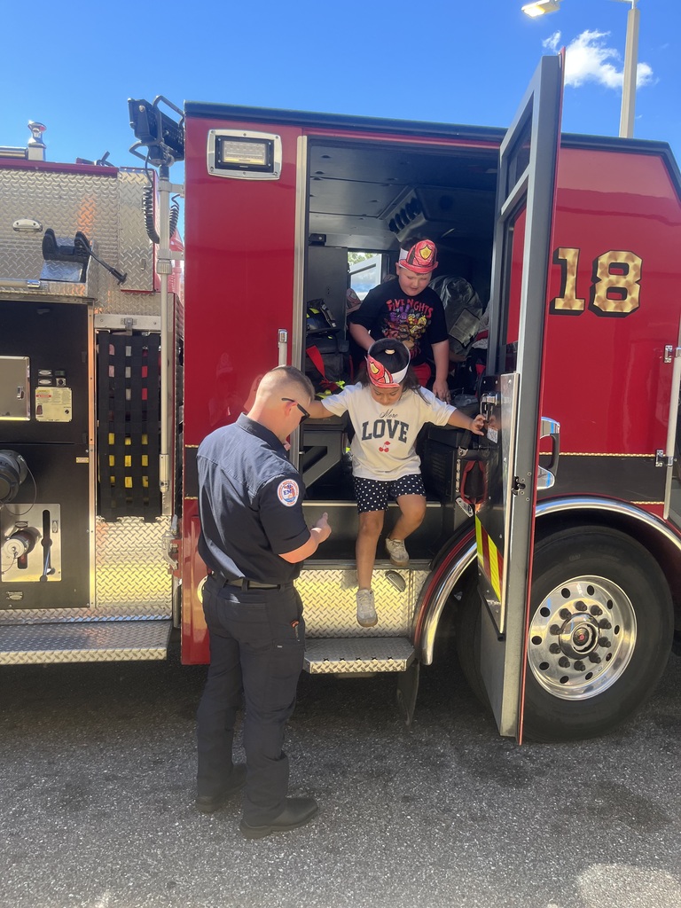 Two students in caps and sneakers step into a red fire truck with open doors.