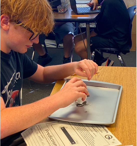 A student with glasses works on an experiment in a tray on a table in a classroom.
