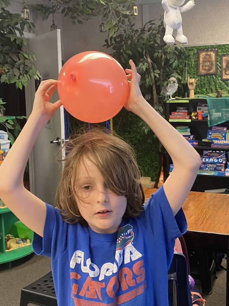 Child with brown hair wearing a blue shirt holds a large orange balloon above their head.