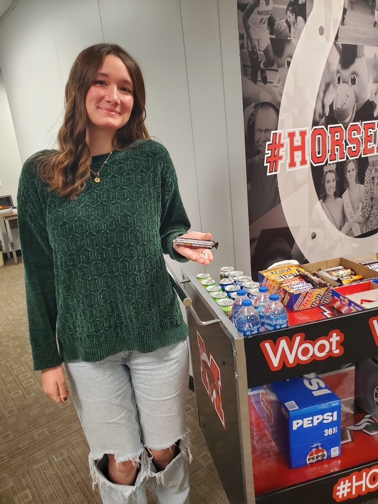 Woman holding candy in front of a display of snacks and drinks with a sign.