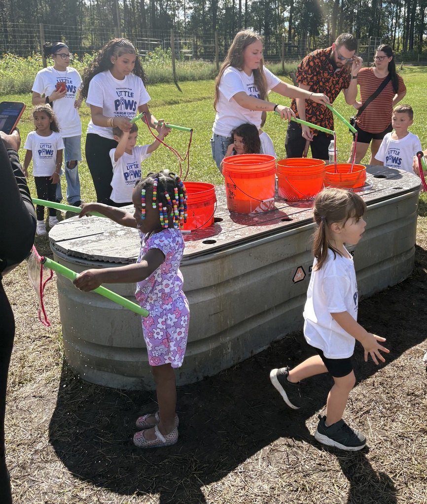 Children wearing matching shirts play with ropes and red buckets on a metal structure.