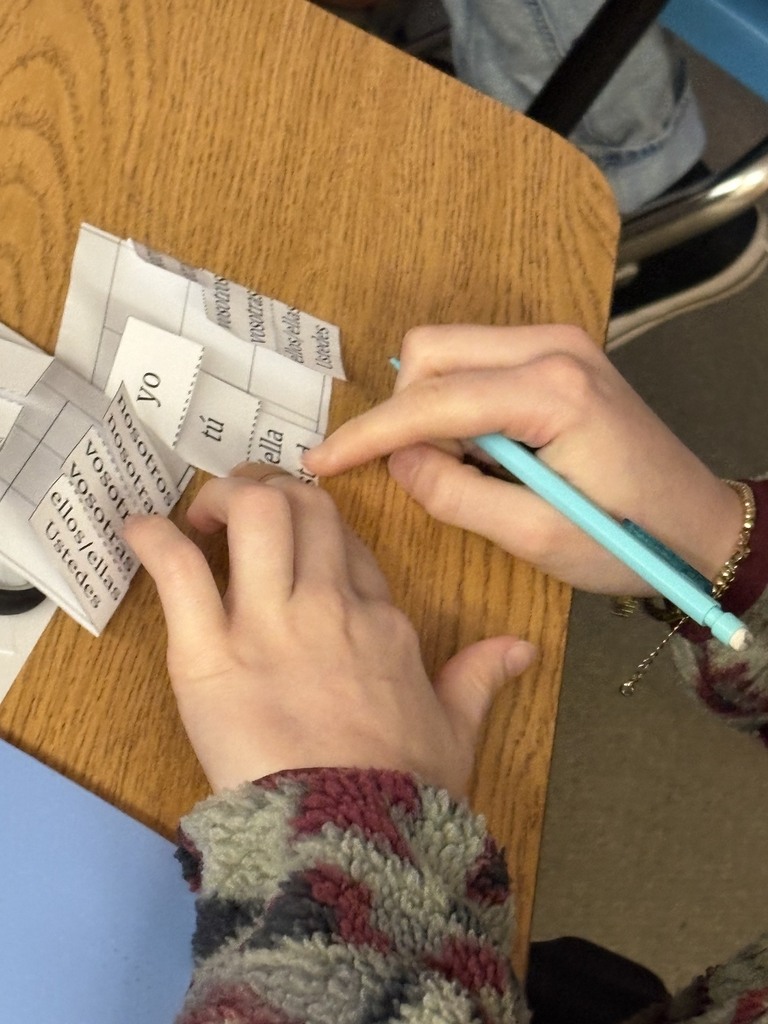 Person uses light blue pen to write on paper with numbers at a desk.