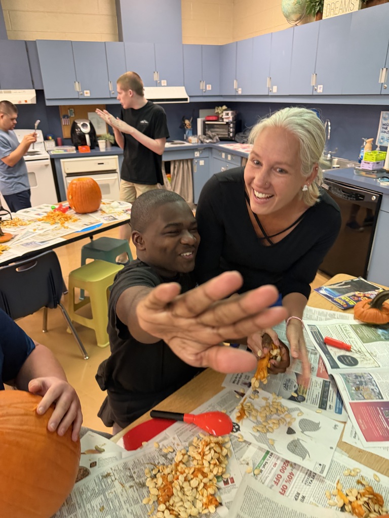 A smiling woman and man carving a pumpkin, surrounded by papers, seeds, and more pumpkins.
