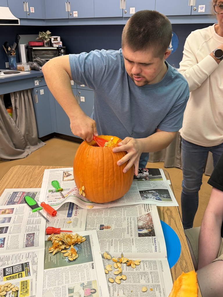 A person in a blue shirt carves a pumpkin on a table covered with newspaper.