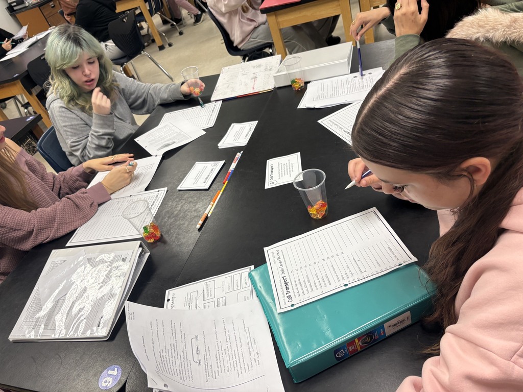 Students seated around a table, each working on papers and using pens and pencils.