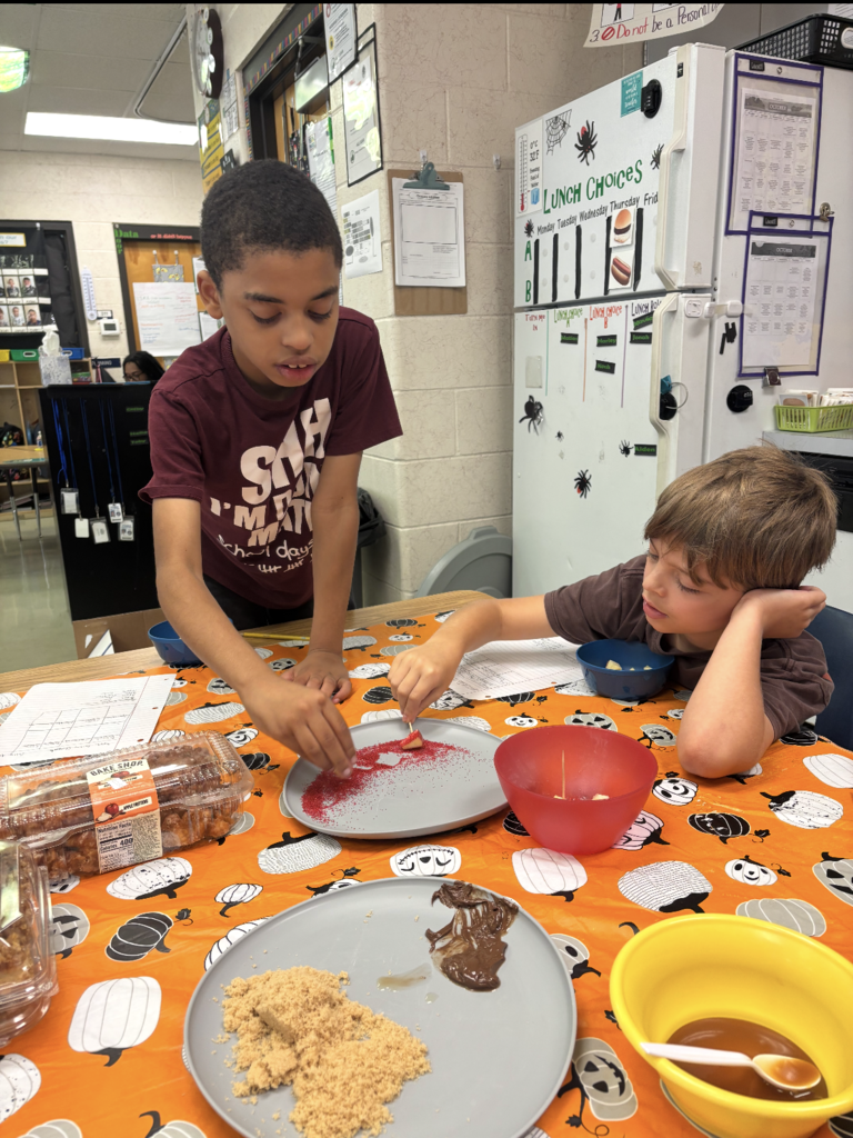 Two children at a table, one cutting something on a plate, another holding a spoon in a bowl.