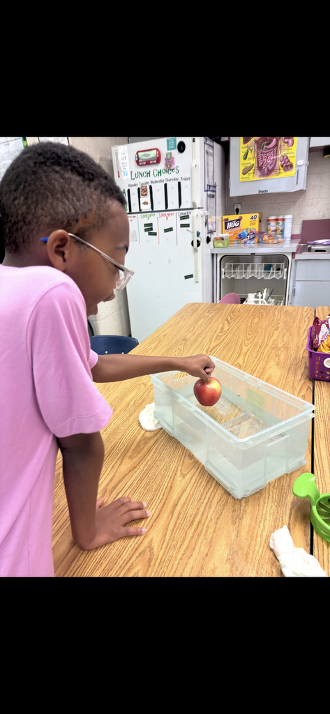 Child in pink shirt holding apple over container, looking downward. 