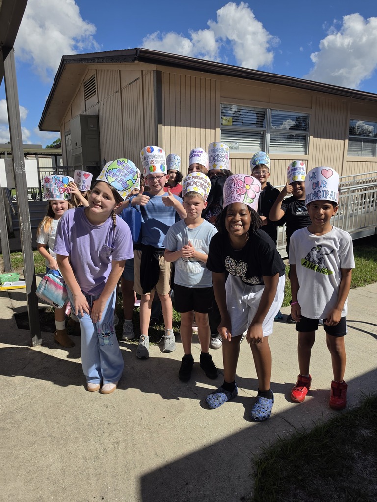 A group of children wearing paper chef hats stands in front of a building with several windows.