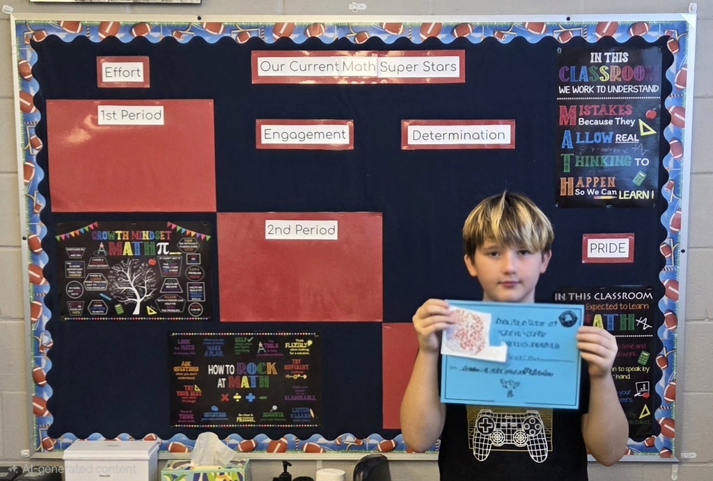 A young boy holds a blue paper up in front of him in front of a bulletin board.