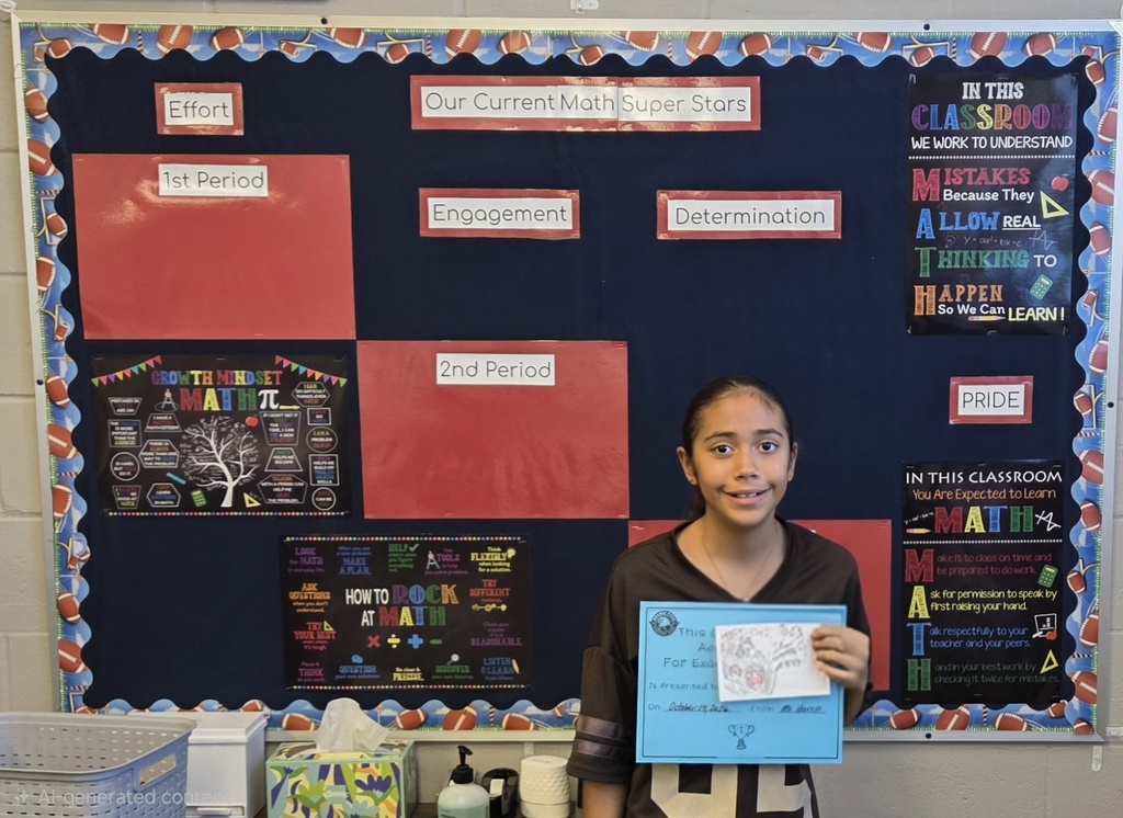 A young girl holds a blue paper in front of a bulletin board with red, black and white squares.