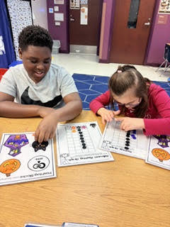 Two children seated at a table, one placing counters on a grid while the other looks on.