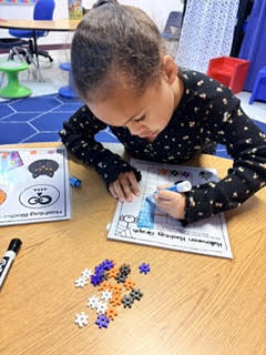 Student leaning over table, working on a puzzle, surrounded by colorful puzzle pieces.