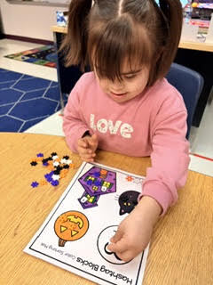 A young girl seated at a table, arranging beads on a paper with fall-themed images.