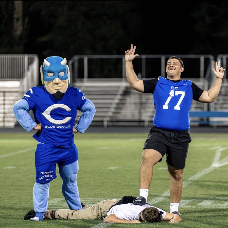 Two people in a mascot costume and another in a blue jersey with a number celebrate.