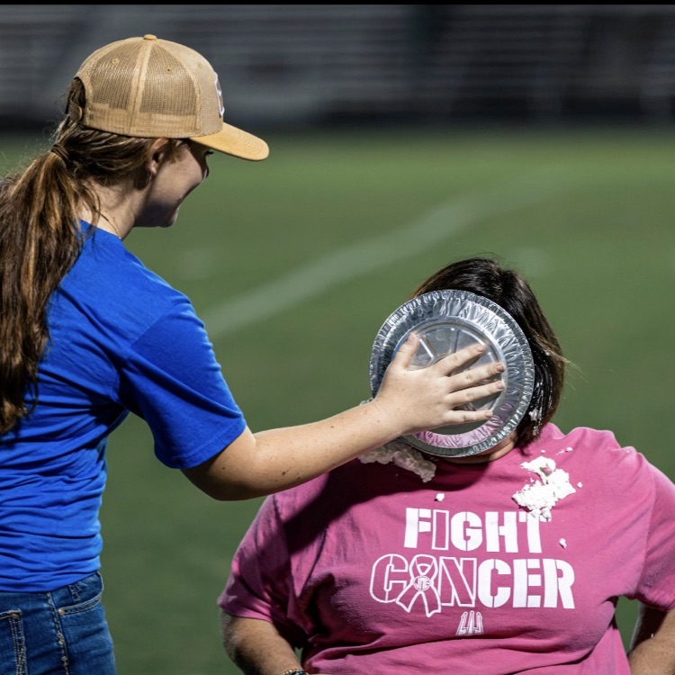 Two people on a field. One holds a frisbee over another's head, who wears a pink shirt.