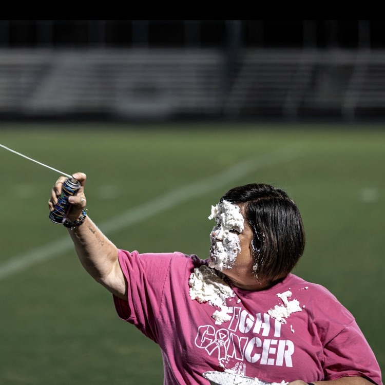 A woman holds a long stick outdoors; another person holds a long stick. Both have white powder on their faces.