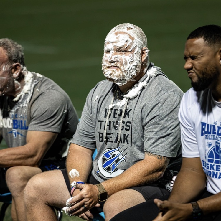 Three men with white powder on their faces sit on a bench at a sports field.
