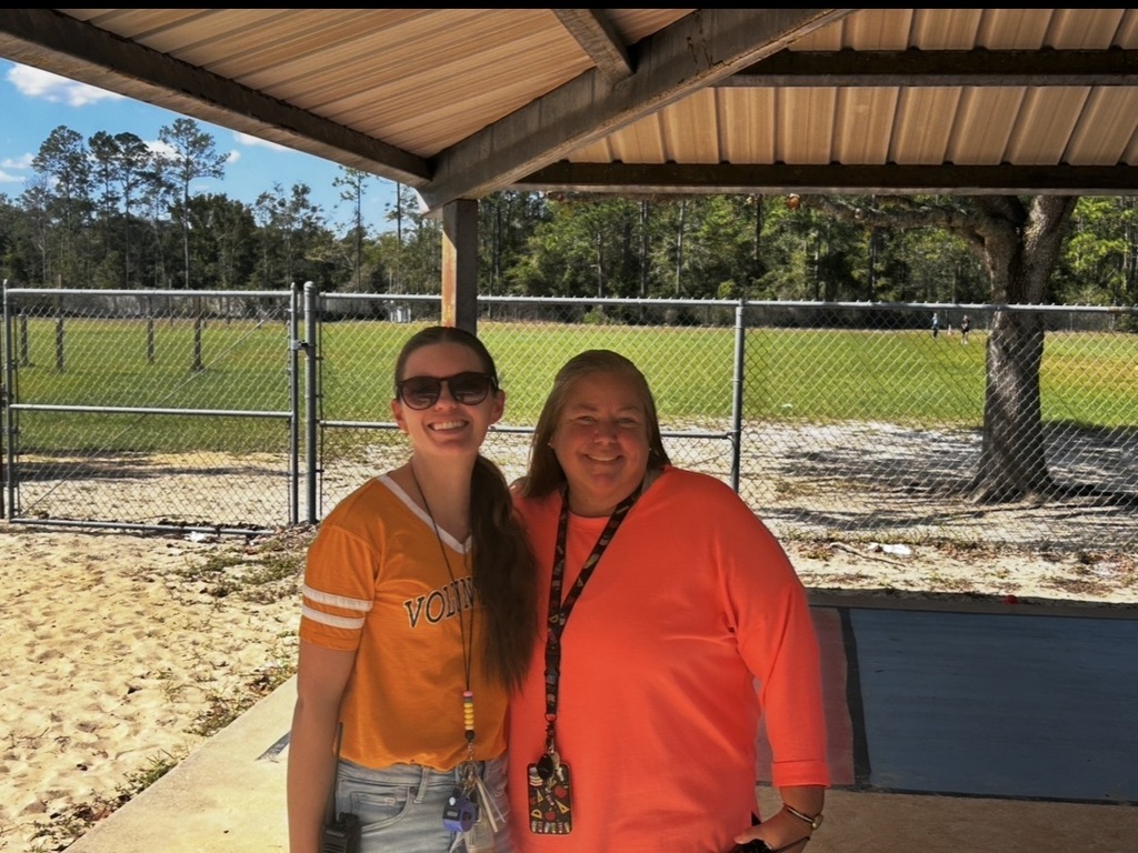Two women standing under a shelter, one in an orange shirt, the other in a yellow shirt.