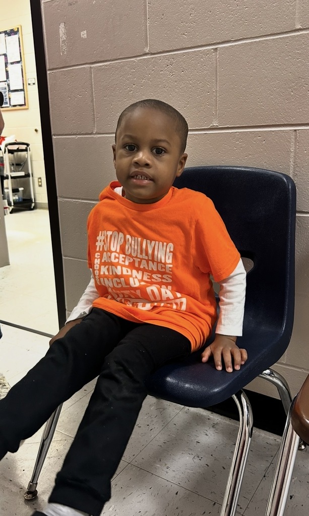 Child wearing orange shirt with '#STOP BULLYING' printed on it sitting on a blue chair.
