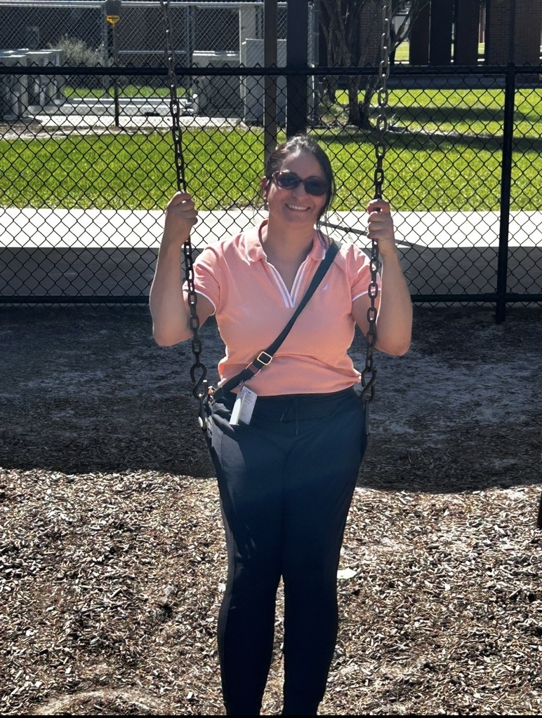 Woman with sunglasses in a pink shirt stands on a swing with a chain attached.