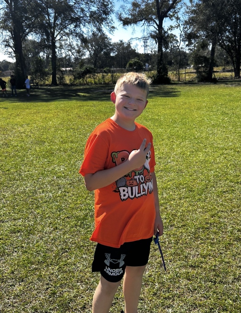 A student in an orange shirt stands in a grassy field