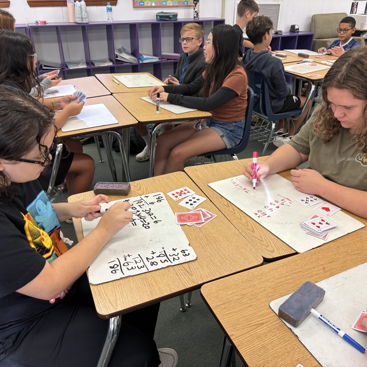 students at desks with white boards and playing cards playing a math game to practice integers