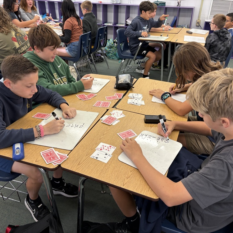students at desks with white boards and playing cards playing a math game to practice integers