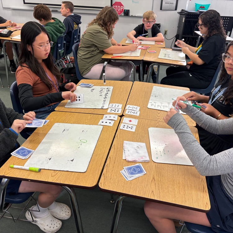 students at desks with white boards and playing cards playing a math game to practice integers