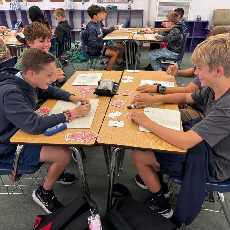 students at desks with white boards and playing cards playing a math game to practice integers