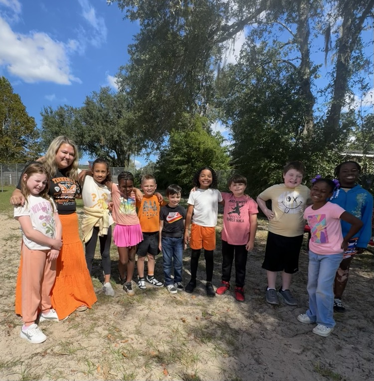 Group of young students, including two adults, pose for a photo in a field with trees.