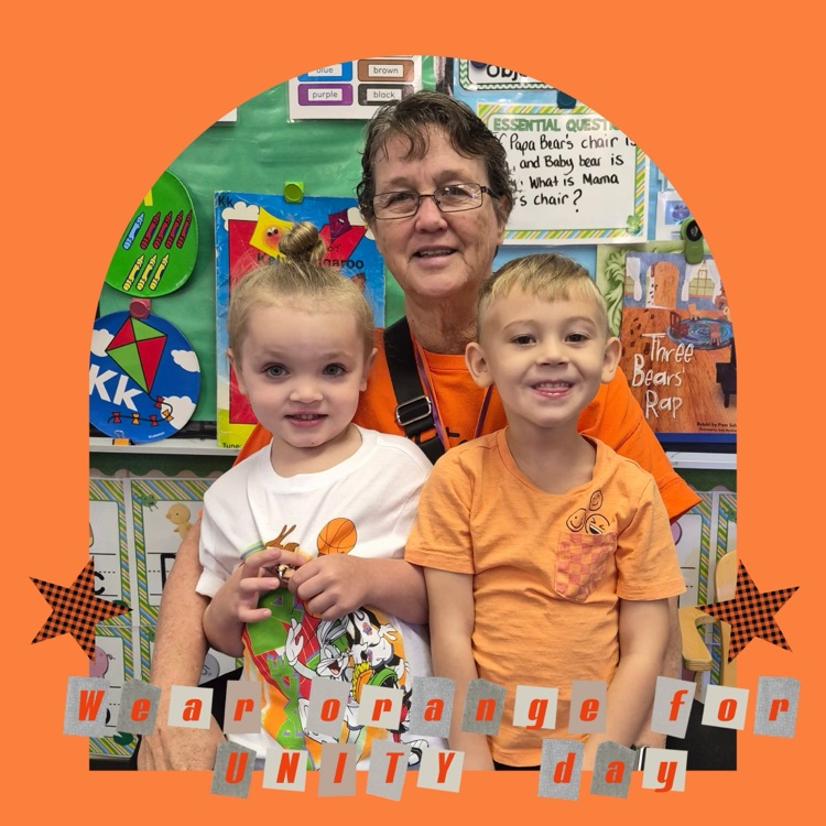 Two young children stand beside a smiling woman; one holds a green object, and the other wears an orange shirt.