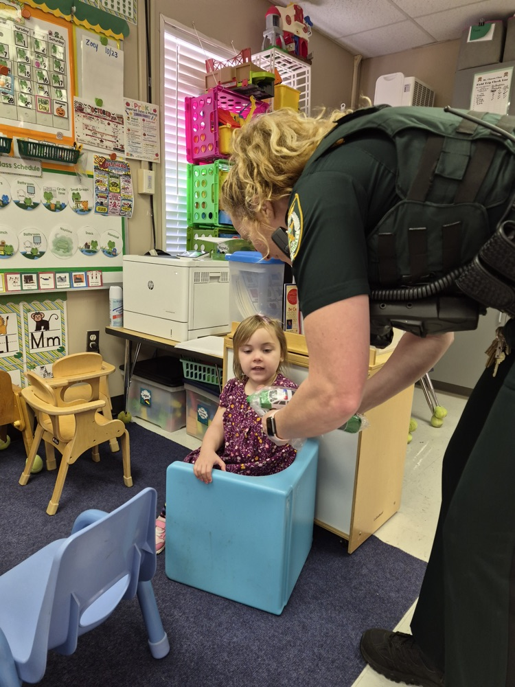 Woman in police uniform hands bracelet to a young girl sitting on a stool.