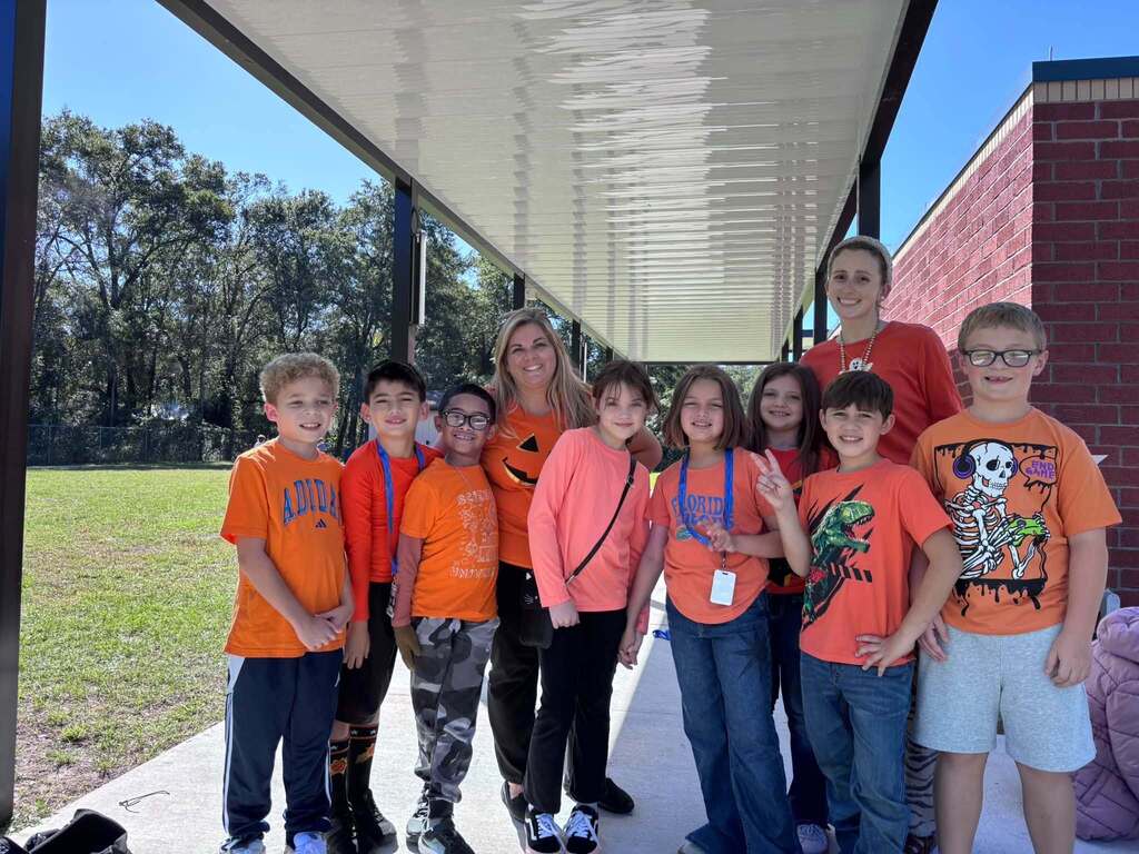 Several students and teachers standing in a hallway, wearing orange shirts and posing for a photo.