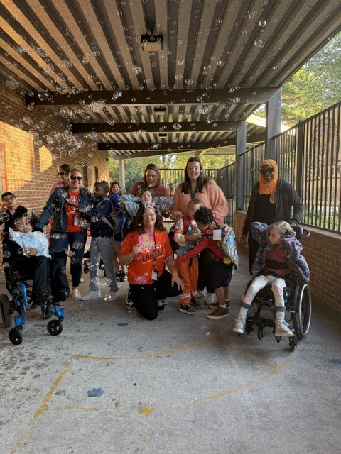 A group of students, some in wheelchairs, pose for a photo under a covered walkway with bubble makers.