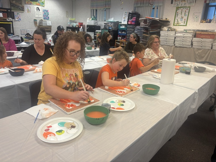 A group of people seated around tables, engaged in painting with brushes and paint on plates.