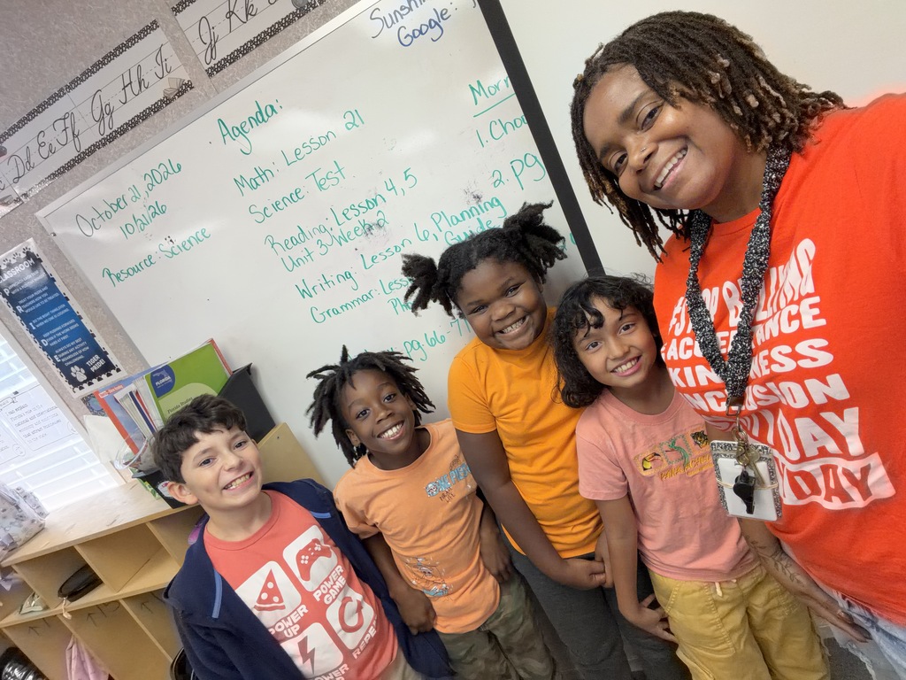Four children and a woman with a lanyard stand in front of a whiteboard.