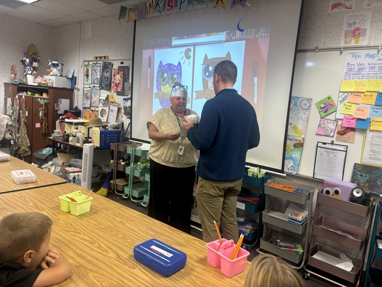 People in a classroom with a projector screen on the wall showing an animated character.