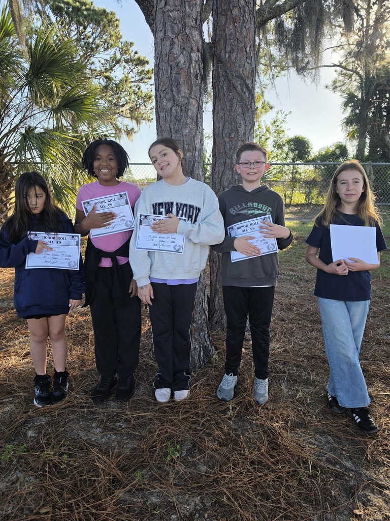 Five children stand in a row under a tree, each holding a white paper and wearing school uniforms.