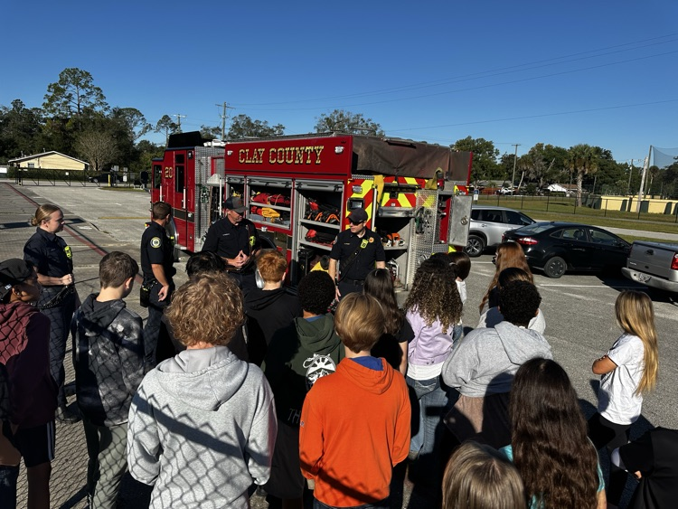 A group of students gathered around a fire truck. Two adults stand near the truck.