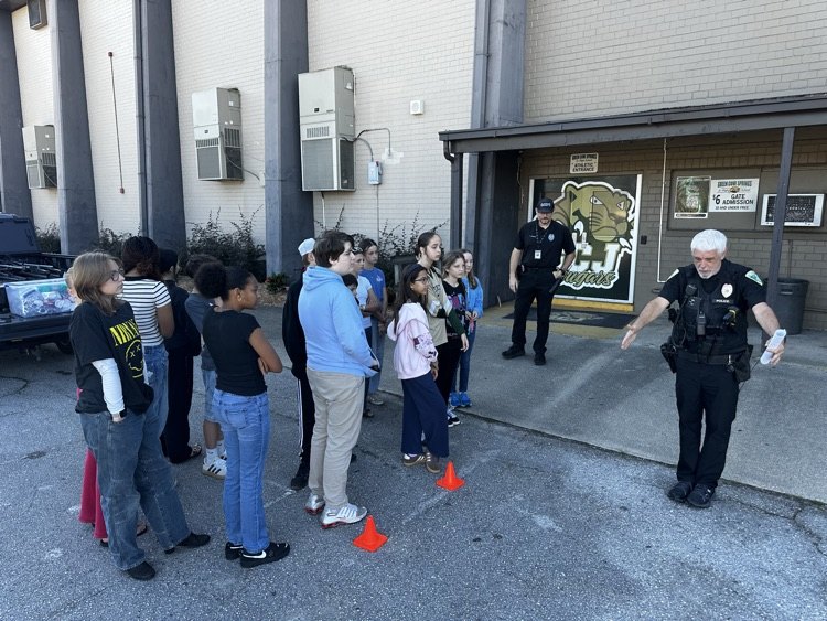 A police officer shows a group of children a traffic safety lesson outside of a building.