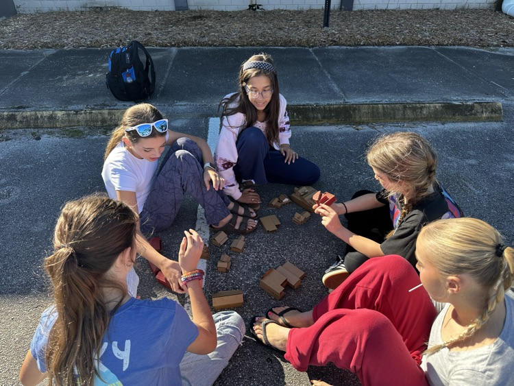 Girls sitting on a street corner, interacting with and talking about small rectangular blocks.