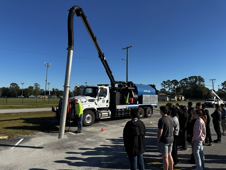 A large white and blue truck with an extended arm is parked in a parking lot.