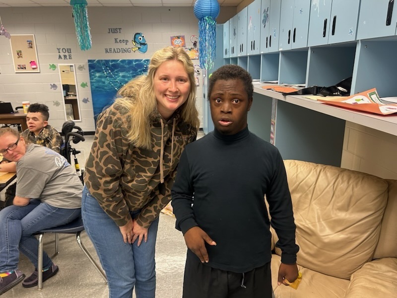 A woman in a camouflage jacket and jeans stands next to a boy in a black turtleneck.