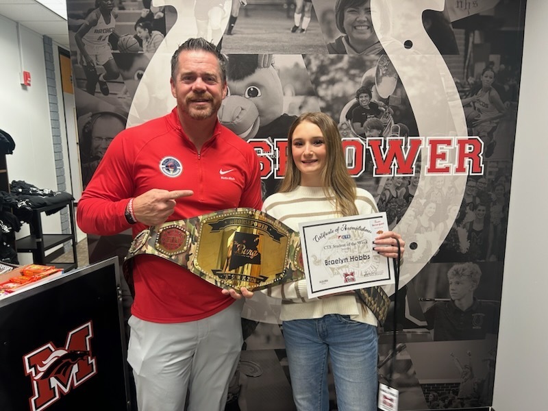 Adult and young woman posing with belt and certificate in front of a large wall mural.