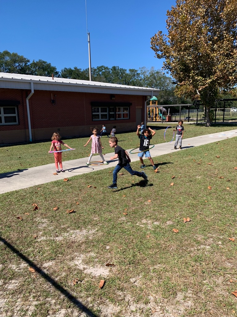 Children play in a field with dried grass, some running and others holding hoops.