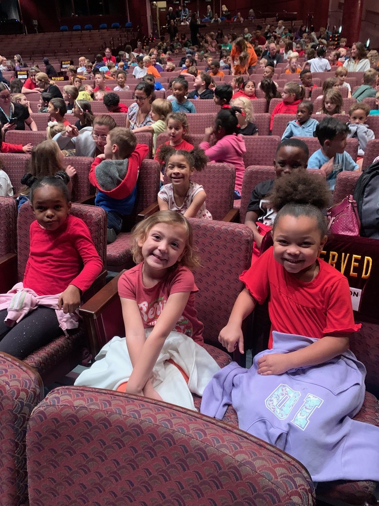 Students seated in theater chairs; one holds a blanket, another holds a stuffed animal.
