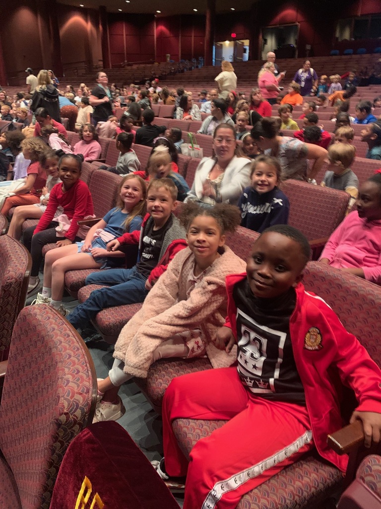 A group of students and teachers seated in an auditorium. Some are smiling, others looking around.